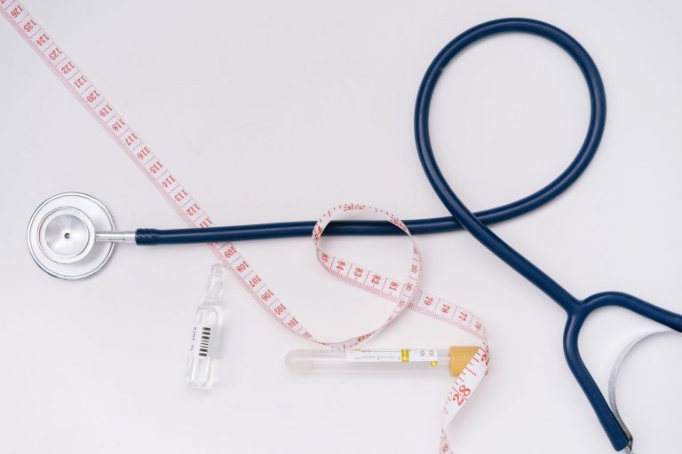 Un estetoscopio, ampolla y cinta métrica sobre un fondo blanco simbolizan lo esencial en salud.